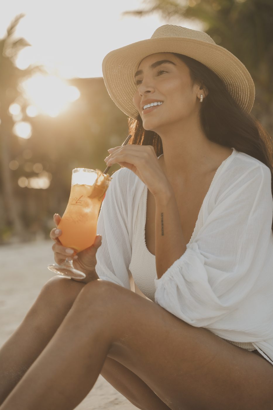 Woman in a sun hat with a FitLine drink on the beach at sunset